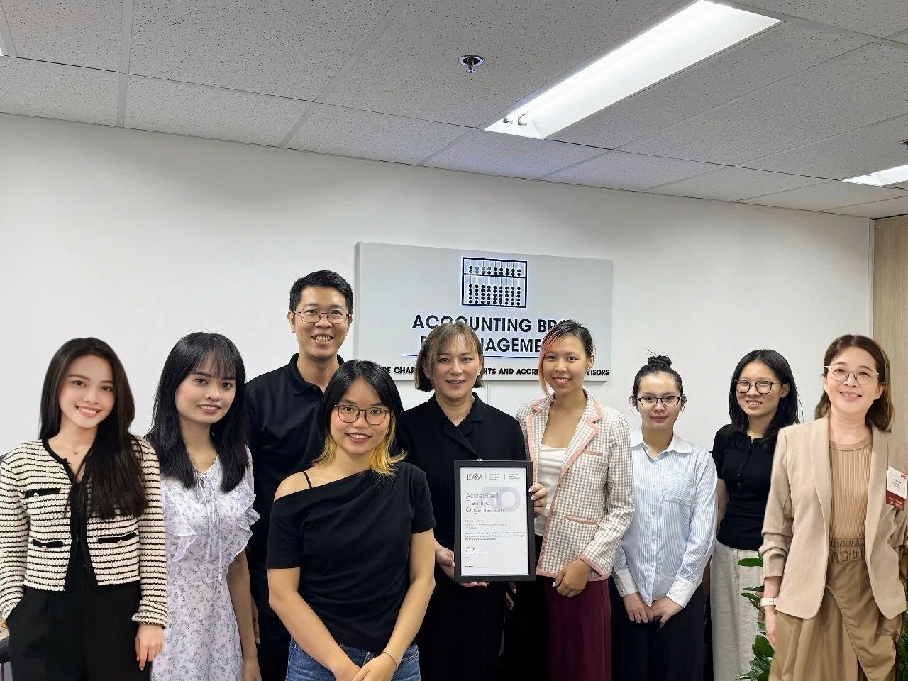 The AccountingBPO team in the Singapore office, standing in front of the Accounting BPO sign and holding ISCA's Accredited Training Organisation certificate.